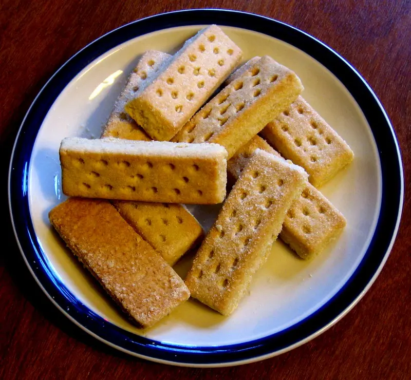 Golden Scottish shortbread fingers, pricked and sugar-dusted, piled on a blue-rimmed plate