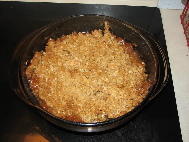 Golden oat crumble topping with bubbling apple juices in a round glass baking dish