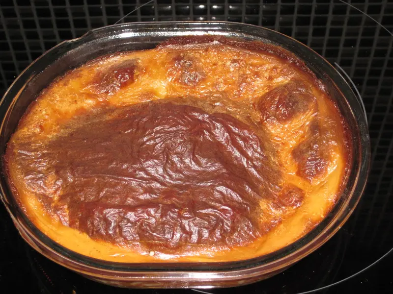 Baked rice pudding in an oval glass dish with a deep golden-brown skin over creamy rice