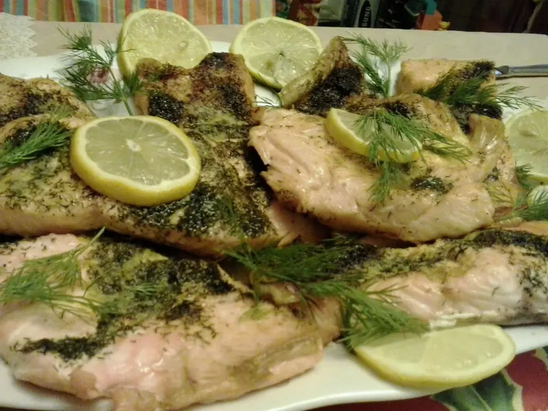 Baked salmon fillets topped with fresh dill and lemon slices on a white serving platter