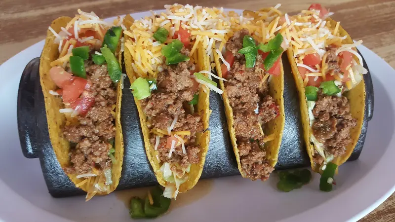 Four crisp taco shells filled with spiced beef mince, grated cheese, tomato and green pepper in a taco holder