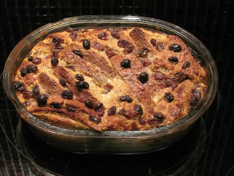 Baked bread and butter pudding with golden custard and plump raisins in an oval glass dish