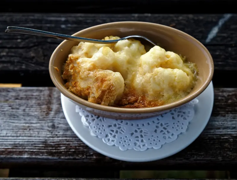 Cauliflower cheese with a golden, bubbling cheese sauce in a small bowl on a rustic wooden table