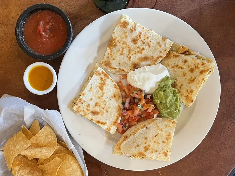 Toasted quesadilla wedges on a plate with pico de gallo, soured cream and guacamole, with salsa and tortilla chips alongside
