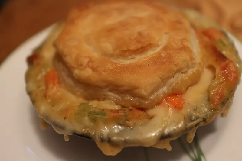 Individual creamy chicken pie with a golden puff pastry lid, sauce bubbling over the edge of the dish