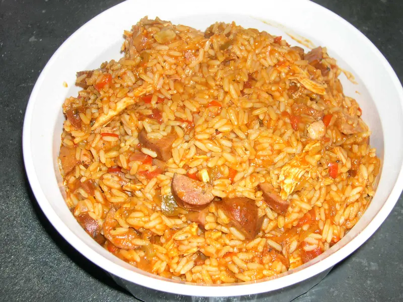 Bowl of tomato-red jambalaya rice with shredded chicken, sliced smoked sausage and peppers