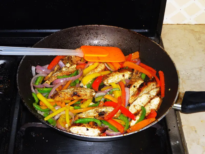 Spiced chicken strips sizzling in a frying pan with sliced red, yellow, orange and green peppers and red onion