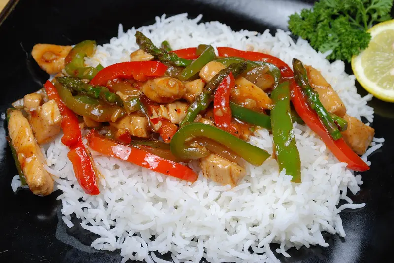 Glossy chicken stir-fry with red and green peppers and asparagus served on a bed of white rice
