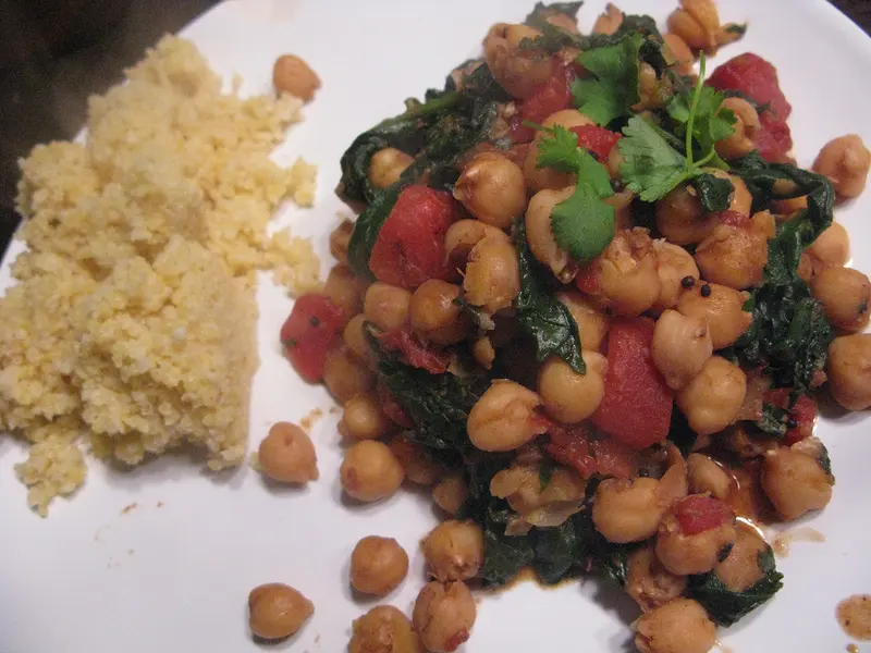 Chickpea and spinach curry with tomatoes and fresh coriander, served beside a mound of grains on a white plate