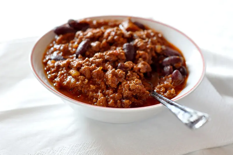 Bowl of beef and kidney bean chilli con carne with a spoon, on a white napkin