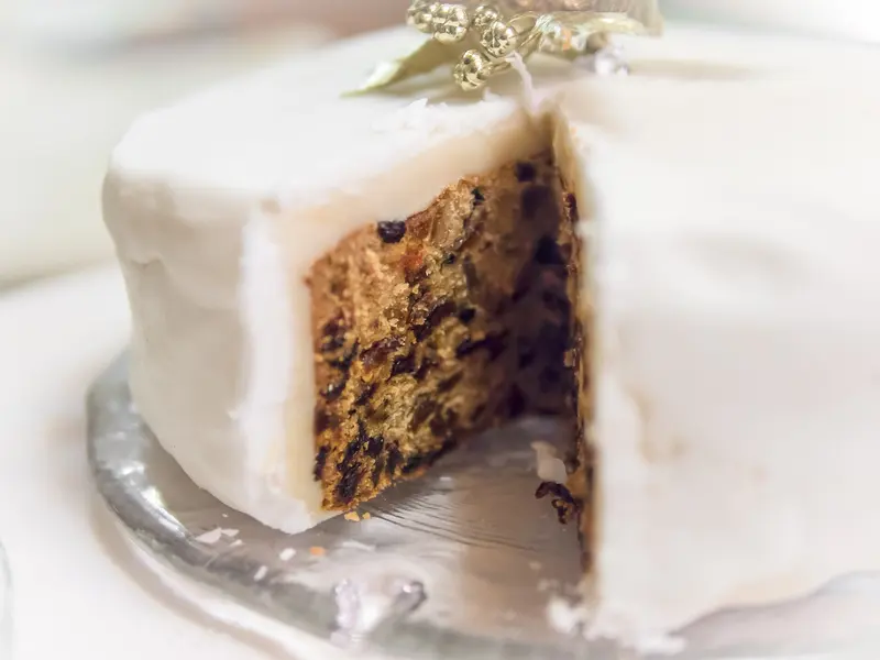 White-iced Christmas cake with a wedge cut out, showing the dark fruit-studded inside