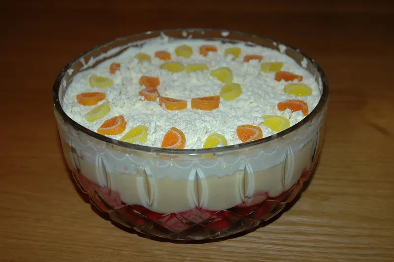 Layered trifle in a cut-glass bowl with red fruit, custard and cream, decorated with orange and lemon jelly slices