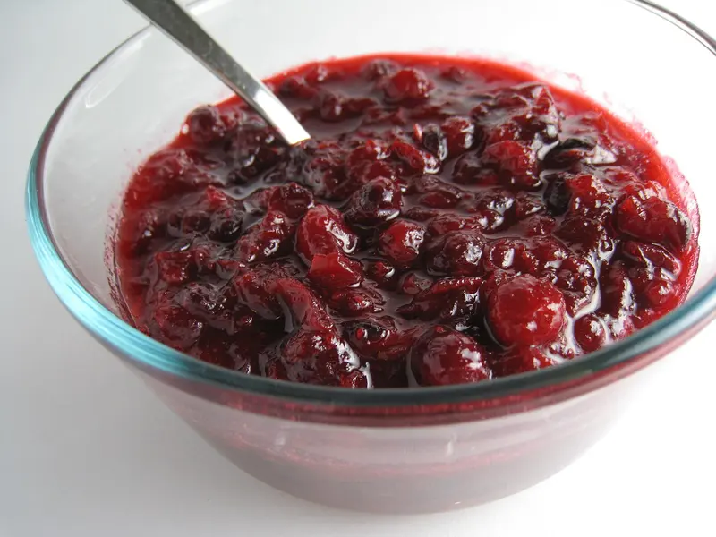 Glass bowl of glossy homemade cranberry sauce with whole burst berries and a spoon