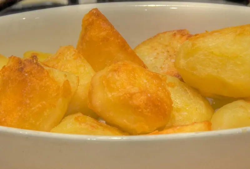 Golden, crisp roast potatoes piled in a white serving dish