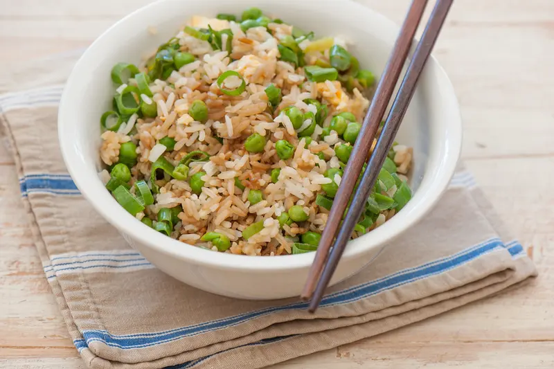 Bowl of egg fried rice with peas and spring onion, chopsticks resting on the rim