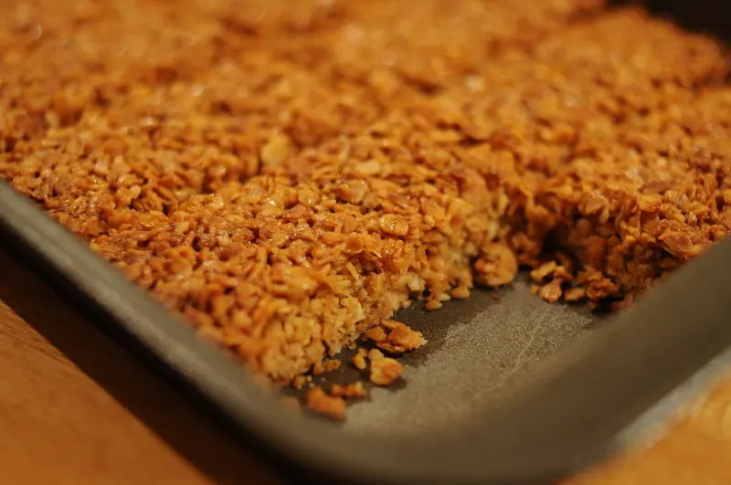 Golden oat flapjack baked in a metal tray, with crisp edges