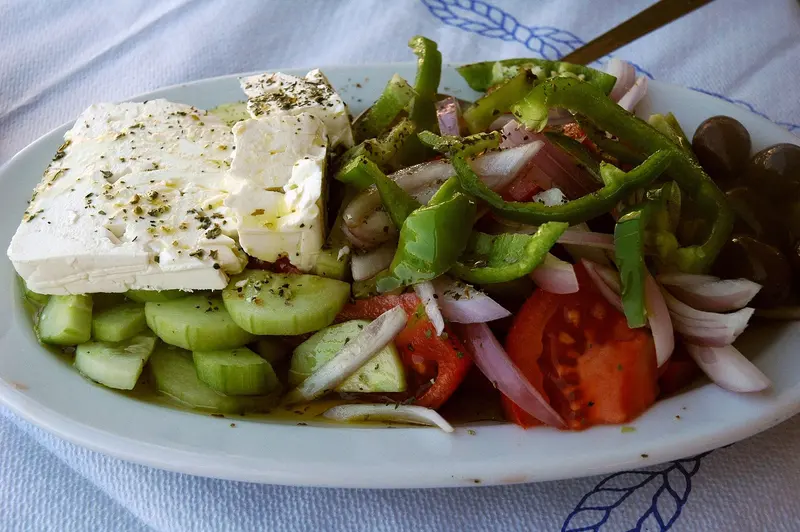 Greek salad of tomato, cucumber, onion and green pepper topped with a slab of feta and oregano on an oval plate