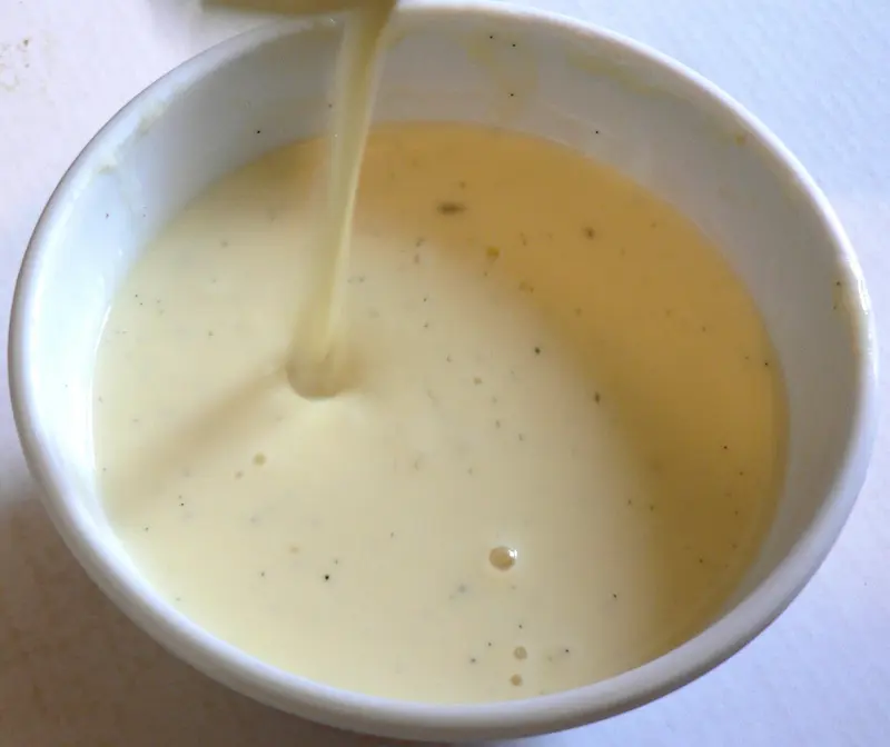 Smooth vanilla custard flecked with vanilla seeds being poured into a white bowl
