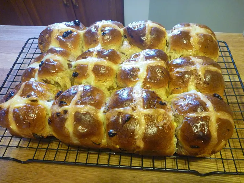 Batch of glossy homemade hot cross buns with piped crosses, cooling on a wire rack