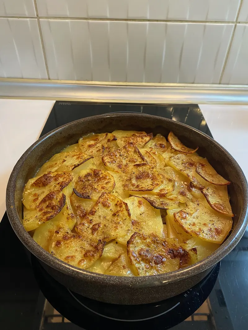Lancashire hotpot in a round dark pot, topped with overlapping golden, crisp-edged potato slices