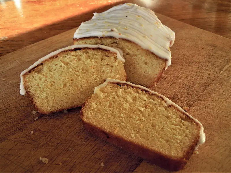 Lemon drizzle loaf cake cut into thick slices on a wooden board, with a thin white lemon glaze on top