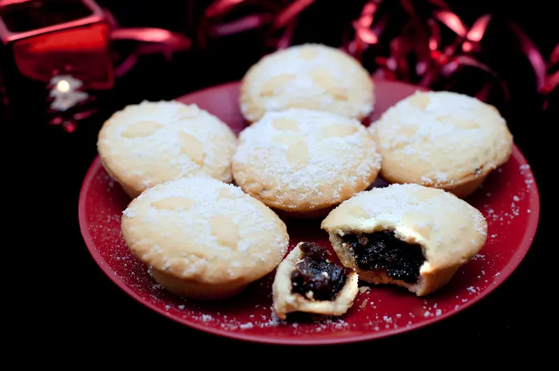 Sugar-dusted mince pies on a red plate, one broken open to show the dark fruity mincemeat filling