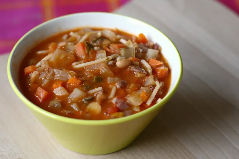 Bowl of thick tomato minestrone with diced carrot, beans and small pasta
