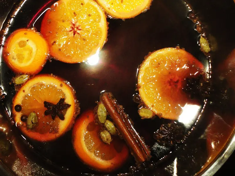 Mulled wine in a pan with floating orange slices, cinnamon sticks, star anise and cardamom pods