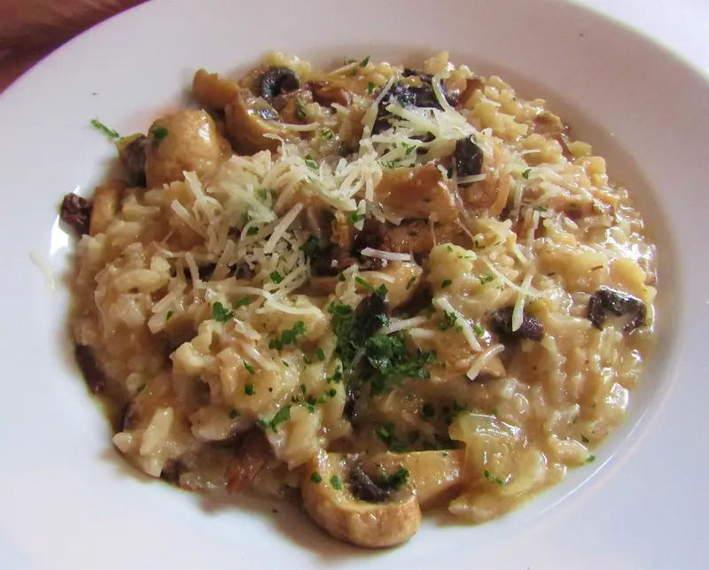 Creamy mushroom risotto in a wide white bowl, topped with grated Parmesan and chopped herbs
