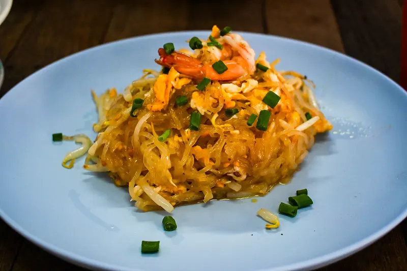 Pad Thai rice noodles with prawns, egg, beansprouts and spring onion piled on a pale blue plate