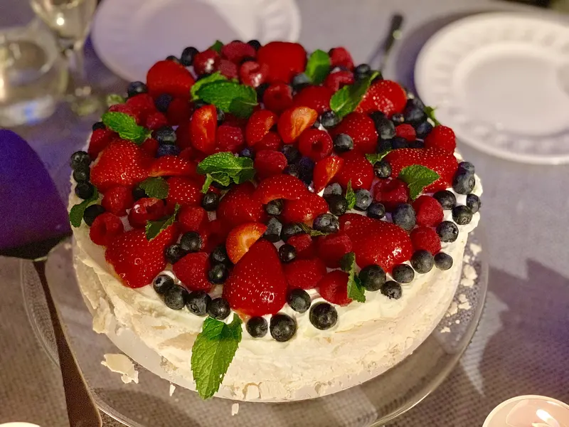 Tall pavlova piled with strawberries, raspberries, blueberries and mint leaves over whipped cream