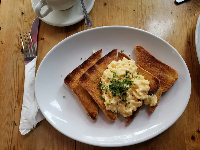 Soft, creamy scrambled eggs sprinkled with chives on triangles of buttered toast, on a white plate