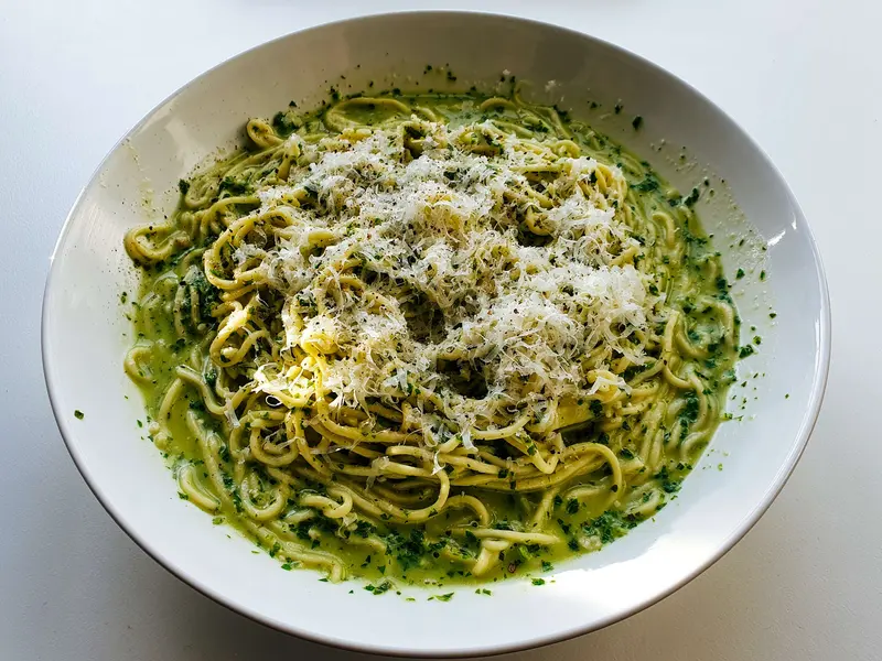 Bowl of thin pasta tossed in bright green basil pesto and topped with grated Parmesan