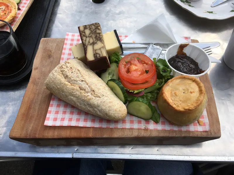 Ploughman's lunch on a wooden board with crusty bread, cheeses, pork pie, pickle, tomato and salad