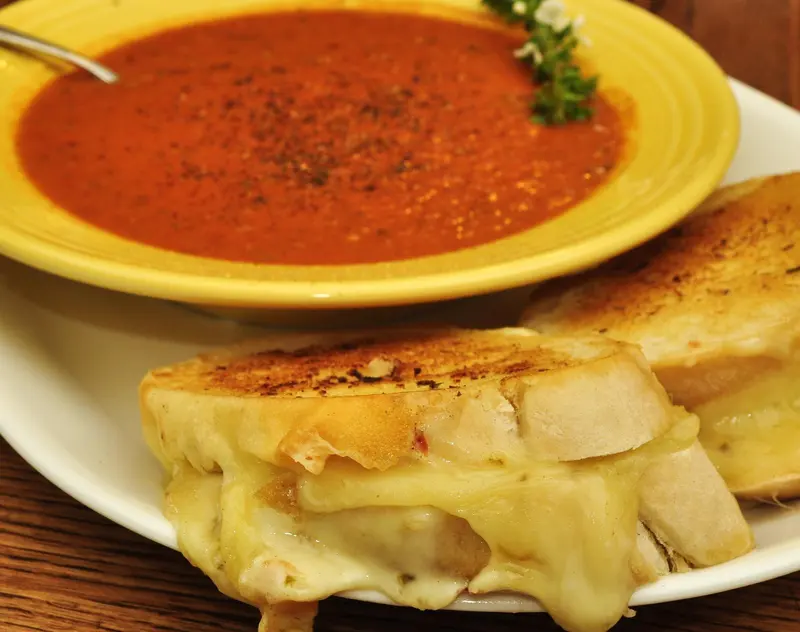 Bowl of rich roasted tomato soup with black pepper and thyme, served with a toasted grilled cheese sandwich