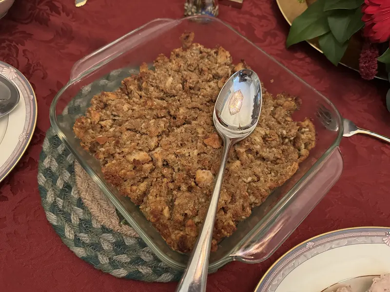Golden baked breadcrumb stuffing in a square glass dish with a serving spoon, on a festive dinner table