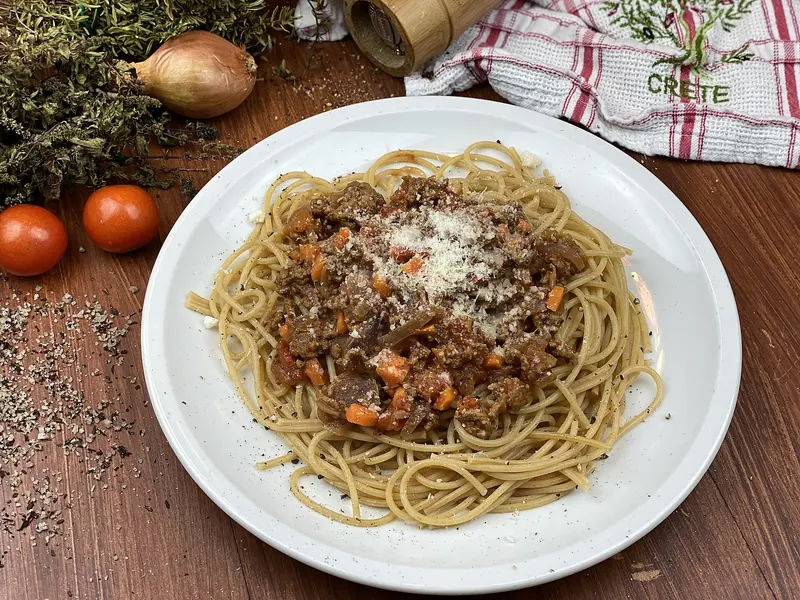 Plate of spaghetti topped with a beef, carrot and tomato ragù and grated parmesan, with fresh tomatoes and herbs alongside