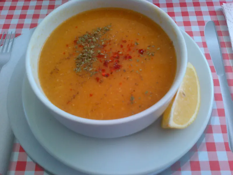 Bowl of smooth orange red lentil soup sprinkled with chilli flakes and dried herbs, served with a lemon wedge