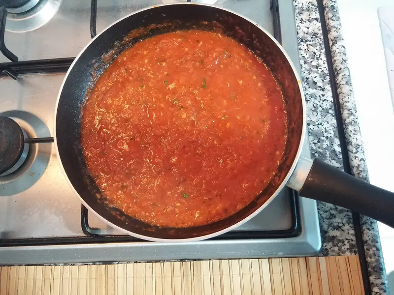 Rich homemade tomato sauce simmering in a non-stick frying pan on a gas hob