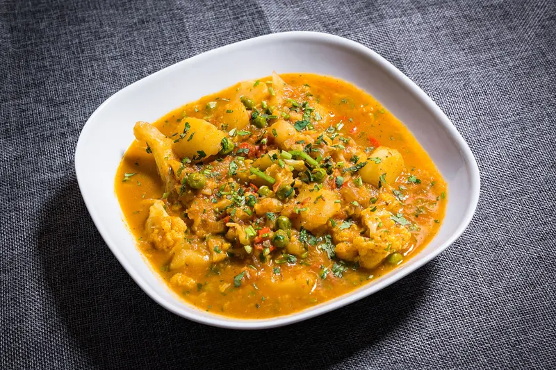 Potato, cauliflower and pea curry in a spiced tomato sauce, scattered with fresh coriander, in a white bowl