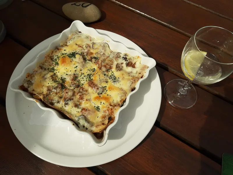 Vegetable lasagne with a golden, bubbling cheese top sprinkled with herbs, in a white fluted baking dish