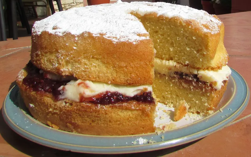 Victoria sponge dusted with icing sugar, cut open to show raspberry jam and buttercream between two golden sponges